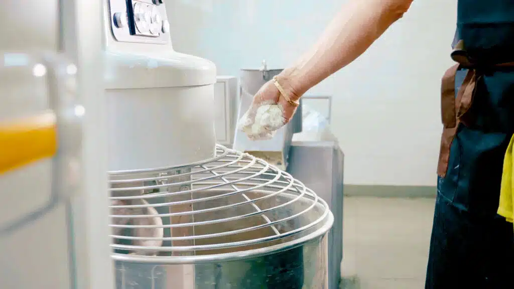 Boulanger qui ajoute de la farine afin de réaliser une pâte dans une boulangerie